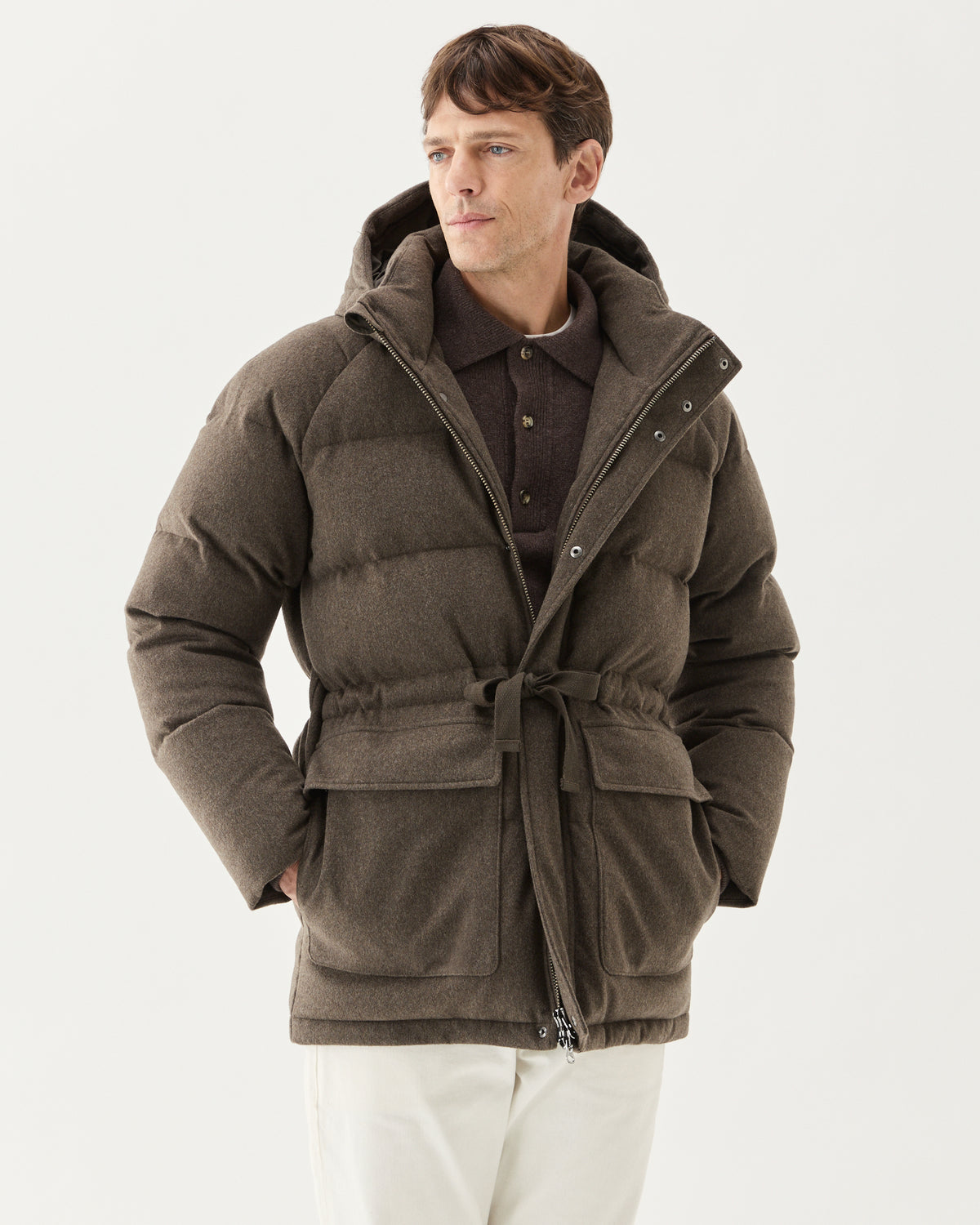 Explorer Down Parka Taupe, worn with the drawstring tied, over a brown knit and white trousers